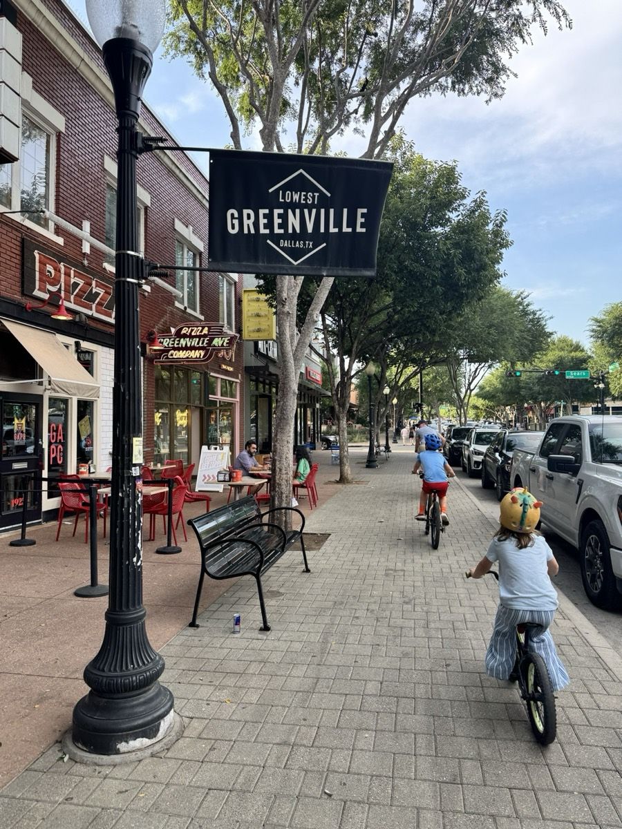 Kids biking down Greenville Avenue past the Lowest Greenville banner